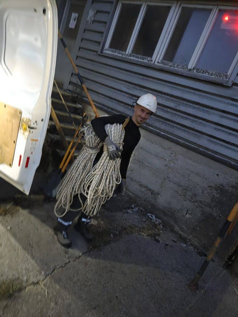 Ouvrier en casque blanc portant des cordes de sécurité devant un fourgon.
